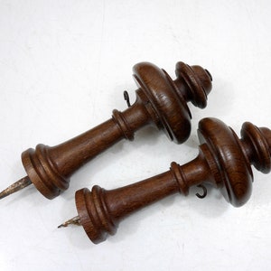 Könnte beinhalten: Zwei Holzfiniale mit dunkelbrauner Oberfläche. Jede Finiale hat eine dekorative Spitze mit einer spitzen Metallspitze unten.
