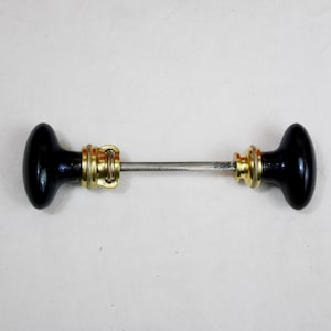 May include: A pair of black ceramic door knobs with brass accents and a metal connecting rod.
