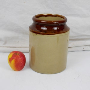 May include: A brown and beige ceramic jar with a brown rim. The jar is empty and is sitting on a white surface.