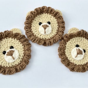 May include: Three crocheted lion head appliques made with brown and beige yarn. Each applique features black button eyes and a white crocheted nose.