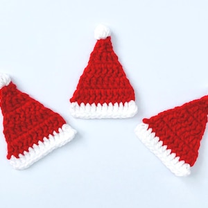 May include: Three small red and white crocheted Santa hats with white pom-poms on top.