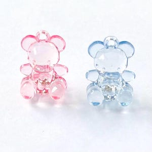 May include: Two clear plastic teddy bear charms, one pink and one blue. The charms have a hole at the top for hanging.