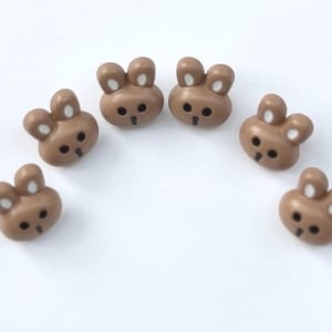 May include: Six brown plastic buttons shaped like bunnies with white ears and black eyes.