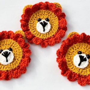 May include: Three crocheted lion appliques made with orange and yellow yarn. Each applique has a white face with black eyes and a black nose.