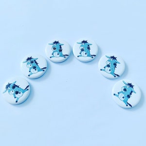 May include: Seven white, circular buttons, each adorned with a cartoon donkey illustration in blue and black. The donkeys are in different poses. These buttons are ideal for craft projects and adding a whimsical element.