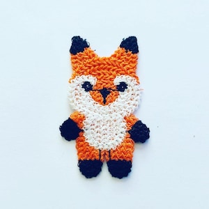 May include: A small orange and white fox figurine made of yarn. The fox has black eyes and a black nose.
