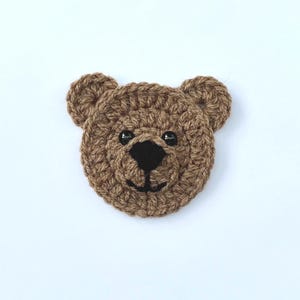 May include: A brown crocheted bear face with black eyes and a black nose.