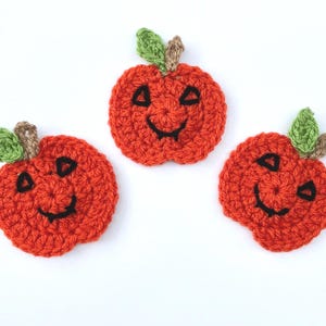 May include: Three crocheted orange pumpkins with black smiling faces and green stems.