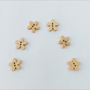 May include: Six wooden buttons shaped like flowers, each with two holes. The buttons are a light brown colour.