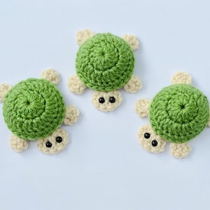 May include: Three crocheted green turtle ornaments with beige accents and black eyes.