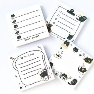 May include: Four white square notepads featuring black line art illustrations of cats, stars, and doodles. One notepad says "Don't forget," another says "To Do List." The other two have a checklist and a decorative border.