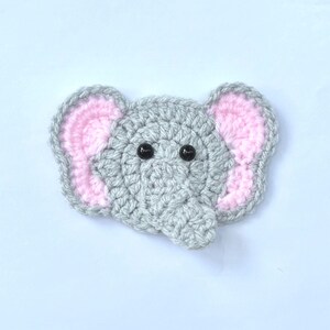 May include: A crocheted elephant applique in grey with pink inner ears and black button eyes. This whimsical design is suitable for baby items, clothing embellishments, or craft projects. The elephant is made with soft yarn.