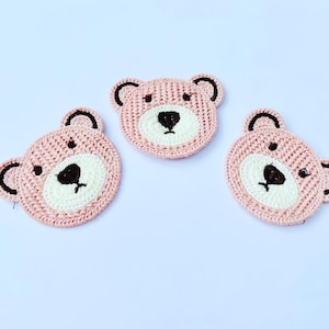 May include: Three pink crocheted bear face appliques with brown embroidered eyes and noses.