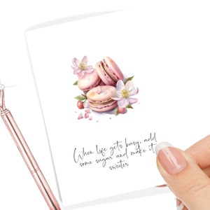 May include: A white card with pink macarons and pink flowers. The text on the card reads "When life gets busy, add some sugar and make it sweeter."