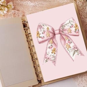May include: A pink planner with a large bow illustration. The bow features a floral pattern with gingerbread men accents. The planner is open, revealing blank pages and a gold spiral binding. The background includes lace and flowers.
