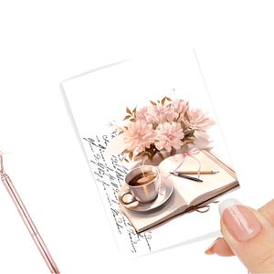 May include: A white card with a pink flower bouquet, a cup of coffee, and an open book with handwritten text. The text on the card reads "...it's just a little bit of magic..."
