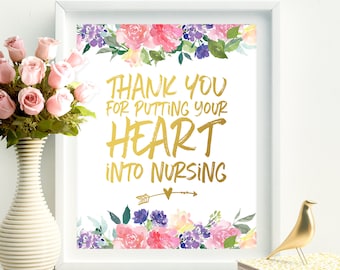 May include: A framed print with the message "Thank You For Putting Your Heart Into Nursing" in gold lettering, surrounded by watercolor floral designs in pink, purple, and yellow. A vase of pink roses and decorative gold birds are also present.
