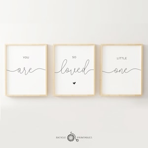Op de afbeelding: Drie ingelijste prints met zwarte kalligrafie op een witte achtergrond. De prints lezen "You are so loved little one".