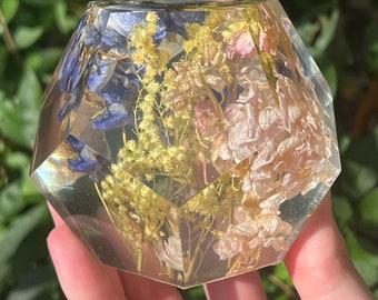 May include: A clear geometric resin paperweight with dried flowers and foliage inside. The flowers are pink, blue, and yellow.