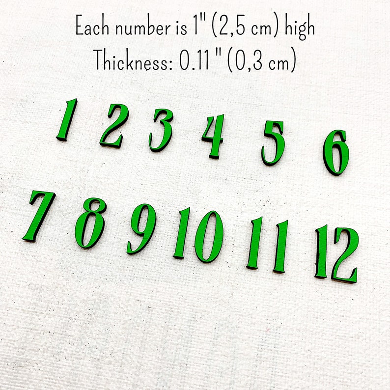 Pu&ograve; includere: Numeri verdi in legno da 1 a 12, ciascuno alto 2,5 cm e spesso 0,3 cm. I numeri sono disposti in due file su una superficie bianca. Il testo sopra i numeri indica le loro dimensioni.