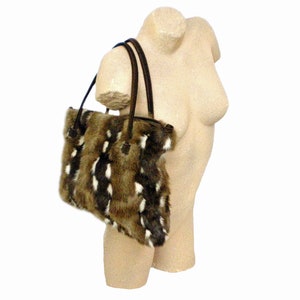 May include: A brown and white faux fur tote bag with dark brown leather handles. The bag is rectangular and has a zipper closure. The bag is displayed on a mannequin.