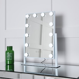 May include: White vanity mirror with a white frame and a rectangular mirror. The mirror has 10 round light bulbs around the perimeter. The mirror is sitting on a white stand with a black cord.