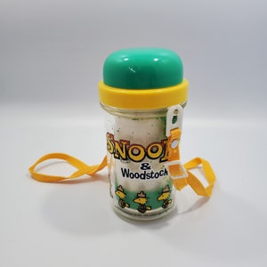 May include: A clear plastic water bottle with a green lid and yellow band. The bottle has a yellow strap and features a graphic of Snoopy and Woodstock. The text on the bottle reads "Snoopy & Woodstock".