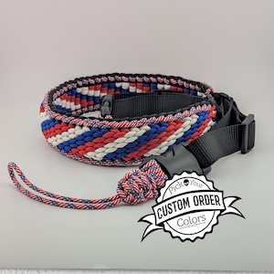May include: Braided strap in red, white, and blue, with black accents and a black buckle. The strap is coiled, with a matching lanyard. The image includes a circular logo that says "Pick Your Custom Order Colors."