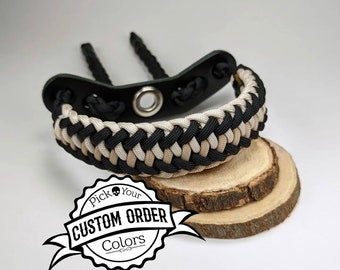 May include: A paracord bracelet featuring a braided pattern in black and beige, attached to a black leather-like component with a central metal grommet. A graphic overlay displays the text "Pick Your CUSTOM ORDER Colors" with a skull icon.
