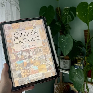 Puede incluir: Una tableta digital que muestra un libro electrónico titulado "Simple Syrups From Scratch" con un collage de imágenes de diferentes jarabes. El texto "Simple Syrups From Scratch" está en blanco y negro con una fuente de estilo manuscrito. El texto "Maria Watkins @livingplanetfriendly" está en la esquina inferior derecha de la pantalla.