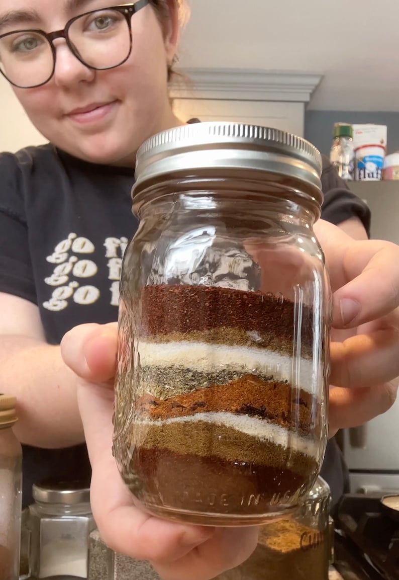 May include: A glass jar filled with layers of different spices, including chilli powder, cumin, oregano, and garlic powder. The jar is labelled "Made in USA".