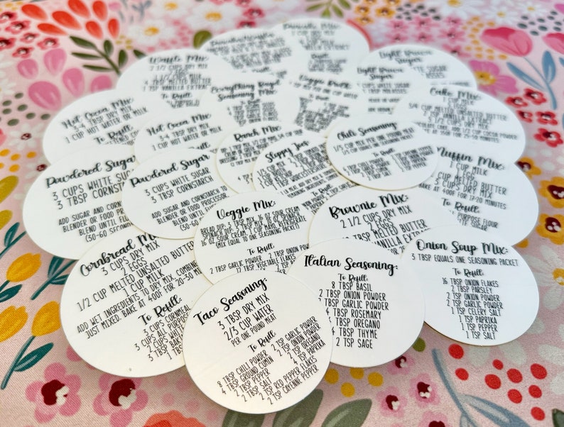May include: A collection of 14 white round labels with black text, each containing a recipe for a different food item, such as cornbread mix, powdered sugar, taco seasoning, and Italian seasoning.