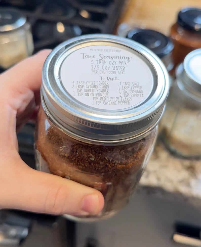 May include: A glass jar filled with brown taco seasoning mix. The lid has a white label with the text "Taco Seasoning: 3 Tbsp Dry Mix 2/3 Cup Water Per One Pound Meat To Reuft 4 Tbsp Chili Powder 2 Tbsp Ground Cumin 1 Tsp Garlic Powder 1 Tsp Onion Powder 1 Tbsp Salt 1 Tbsp Pepper 1 Tsp Oregano 2 Tsp Paprika 1 Tsp Red Pepper Flakes 1 Tsp Cayenne Pepper".