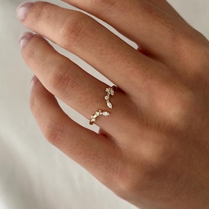 May include: A gold ring featuring a delicate design of small diamonds set in a curved shape. The ring is open on one side, making it adjustable.