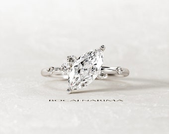 Puede incluir: Un anillo de compromiso de oro blanco con un diamante de talla marquesa y diamantes más pequeños en la banda.
