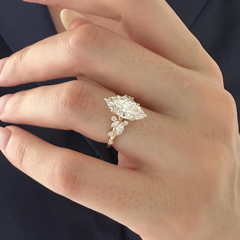 May include: A gold engagement ring with a large marquise-shaped diamond and smaller diamonds set in a floral design.