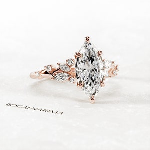 May include: A rose gold engagement ring with a marquise-shaped diamond center stone and smaller diamonds set in a floral design.