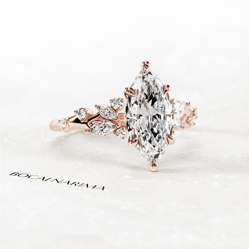 May include: A rose gold engagement ring with a marquise-shaped diamond center stone and smaller diamonds set in a floral design.