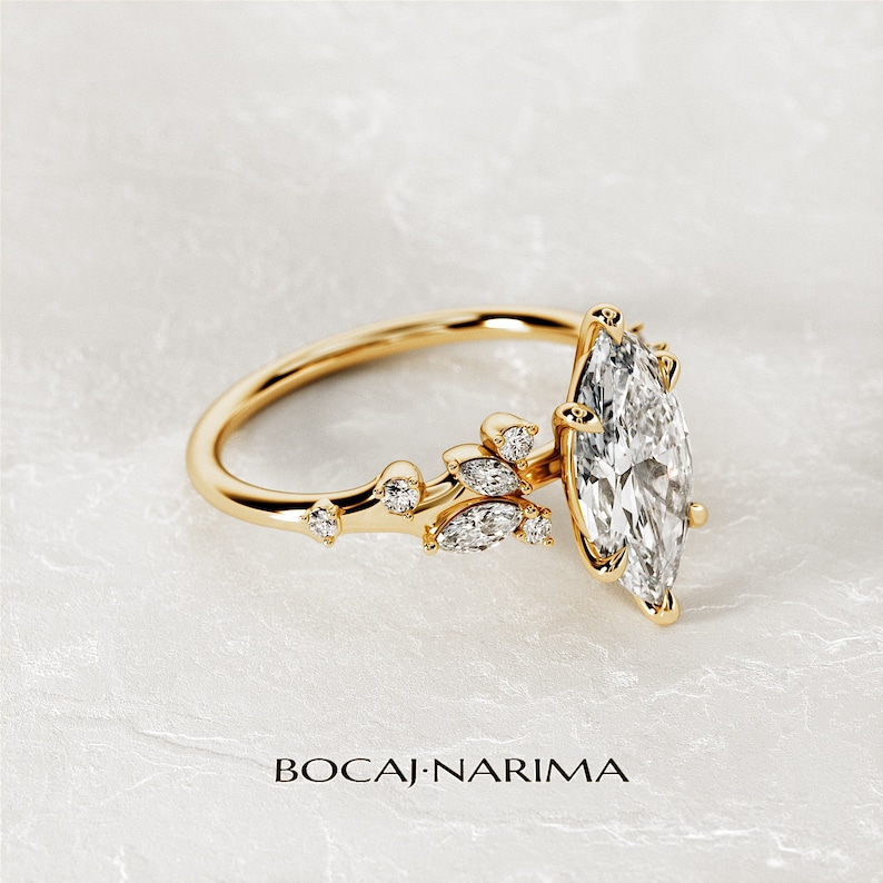 May include: A gold ring with a marquise-shaped diamond and a delicate floral design. The ring features a cluster of smaller diamonds set in a leaf-like pattern.