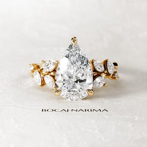 Puede incluir: Un anillo de compromiso de diamante de forma pera con una banda de oro. El anillo presenta un gran diamante de forma pera en el centro, rodeado de diamantes de forma pera m&aacute;s peque&ntilde;os. El anillo est&aacute; engastado en un delicado dise&ntilde;o floral.
