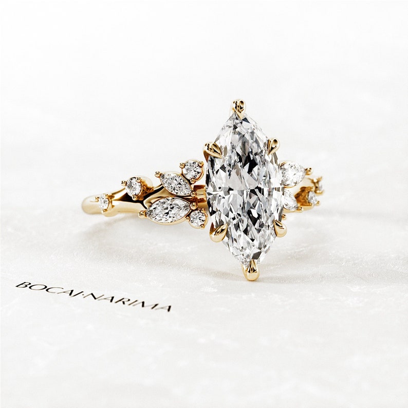 May include: A gold engagement ring with a large marquise-shaped diamond and smaller diamonds set in a floral design.