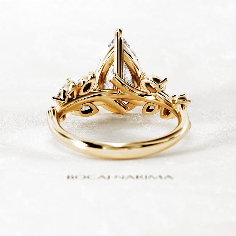 Puede incluir: Un anillo de compromiso de oro en forma de pera con un delicado dise&ntilde;o floral. El anillo presenta una piedra central en forma de pera y piedras redondas m&aacute;s peque&ntilde;as engastadas en el dise&ntilde;o floral.