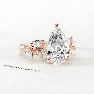 Puede incluir: Un anillo de compromiso de diamante de forma pera engastado en oro rosa con un delicado dise&ntilde;o floral. El anillo presenta una gran piedra central de forma pera y diamantes m&aacute;s peque&ntilde;os engastados en la banda.