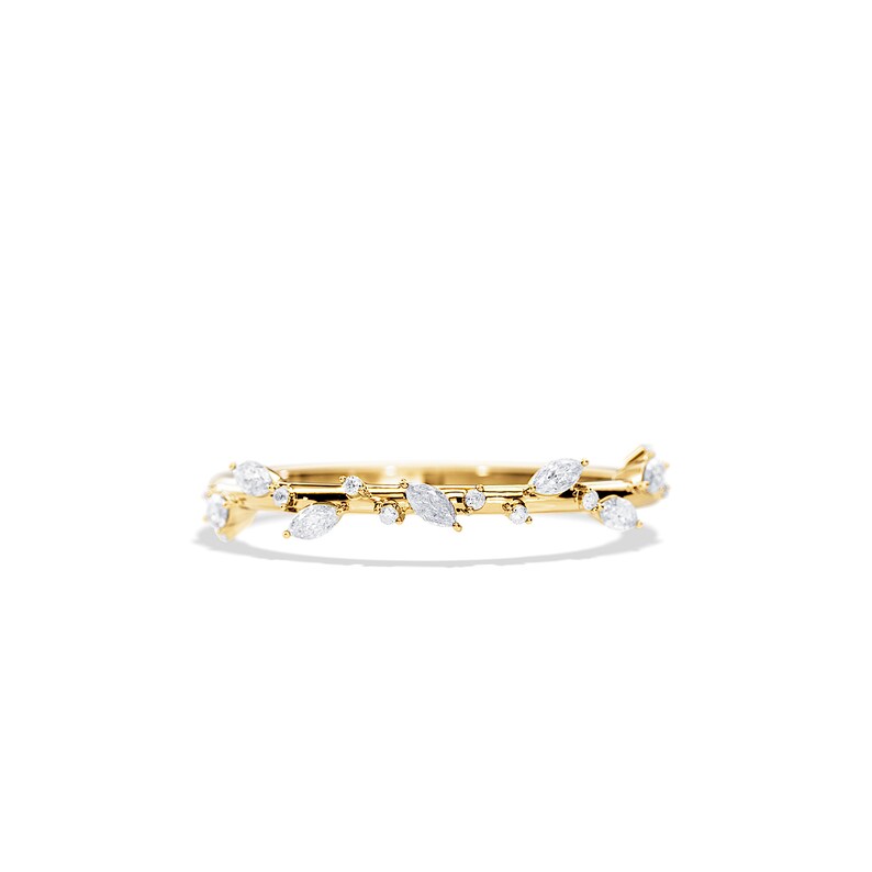 May include: A delicate gold ring featuring a leaf and vine design. The ring is adorned with marquise-cut and round-cut white gemstones, creating a nature-inspired aesthetic. The ring is set against a white background.