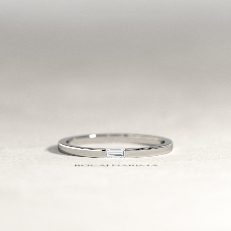 May include: A thin silver band with a small rectangular diamond set in the center.