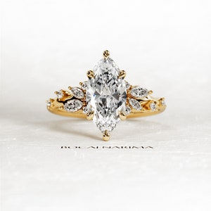 May include: A gold engagement ring with a large marquise-shaped diamond surrounded by smaller diamonds. The ring has a delicate floral design.