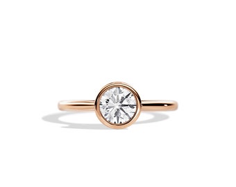 May include: A rose gold engagement ring with a bezel-set round diamond.