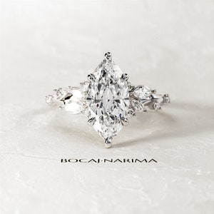 May include: A silver engagement ring with a large marquise-shaped diamond surrounded by smaller diamonds. The ring has a delicate floral design.