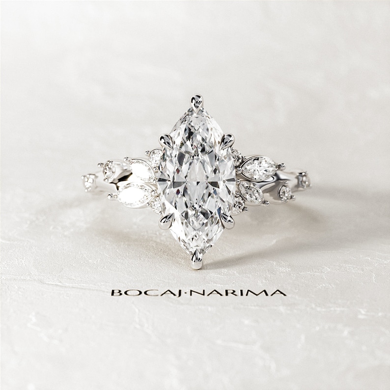 May include: A silver engagement ring with a large marquise-shaped diamond surrounded by smaller diamonds. The ring has a delicate floral design.