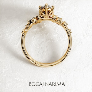May include: A gold ring with a large, round, clear gemstone in the center. The ring has a delicate, floral design with smaller gemstones on the band.